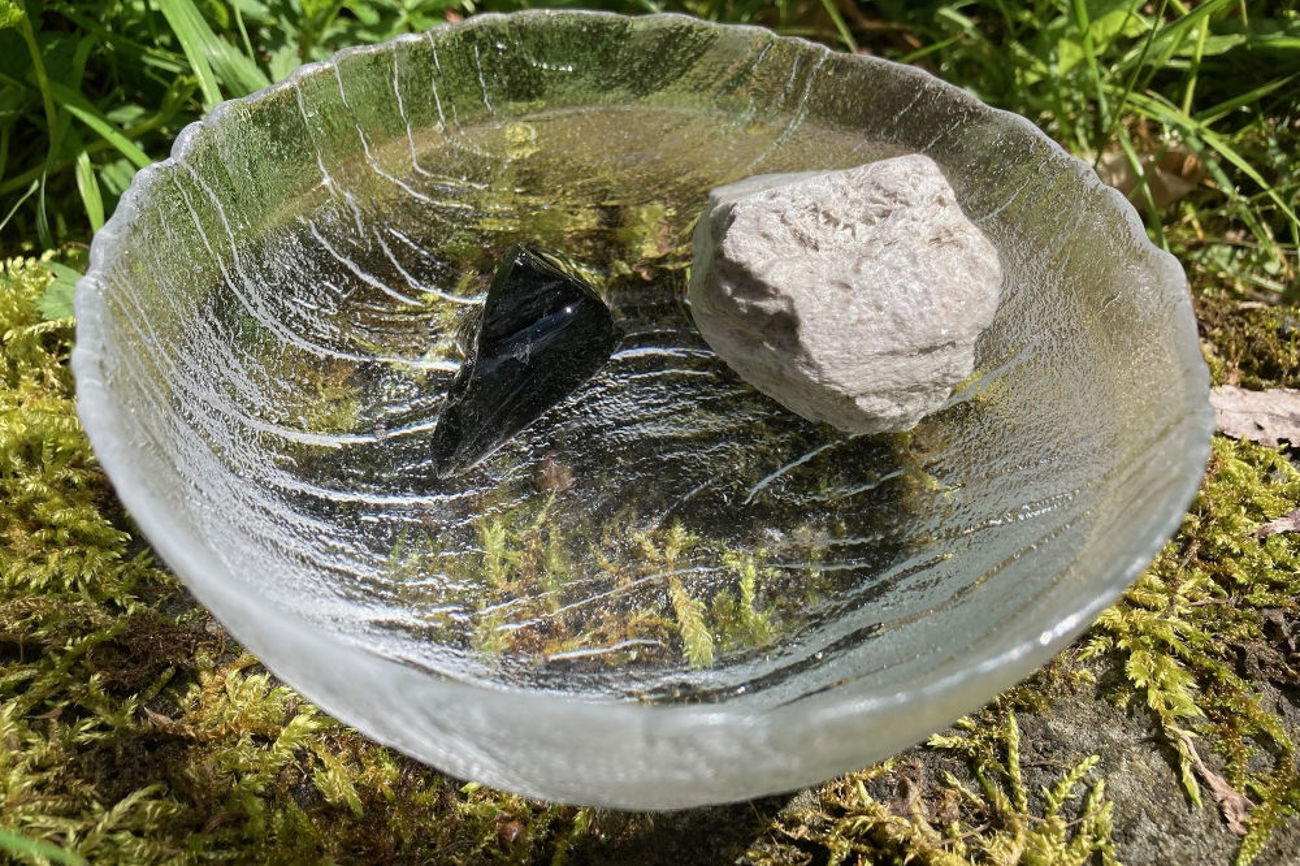 Der leichte Bimsstein schwebt im Wasser, wohingegen beim spitzen Obsidian nur die scharfe Spitze aus der Wasserschale ragt. | Foto: Annette Spitzenberg